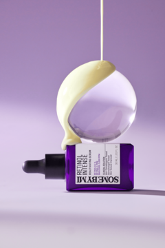 Fioletowe serum SOME BY MI Retinol Intense z kroplomierzem, z żółtym płynem wylewanym na szklaną kulę.
