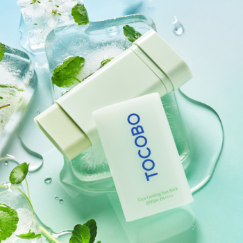 Dwa zielone sztyfty Tocobo Cica Cooling Sun Stick SPF 50+ na mokrej powierzchni z lodem i listkami mięty.