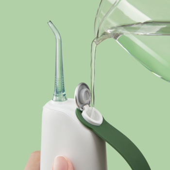 Zbliżenie na irygator dentystyczny Oclean W10, ręka wlewa wodę do zbiornika. Białe urządzenie z zielonymi detalami.