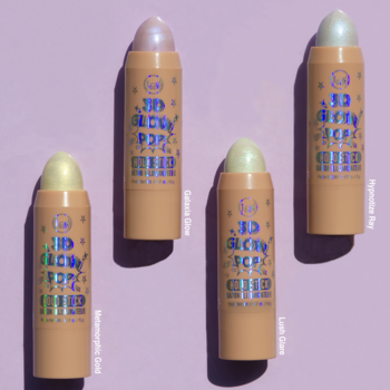 Cztery holograficzne rozświetlacze J.Cat Beauty 3D Glow Pop Holo Stick (róż, zieleń, złoto, biel) na fioletowym tle.