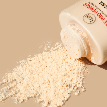 Zbliżenie na jasny sypki puder matujący Banana Luxe Pro Powder, wysypany z beżowego pojemnika na gładkie beżowe tło.