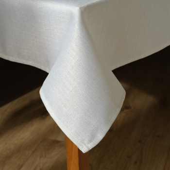 Biały lniany obrus, widok z bliska na złożony róg. Widoczna delikatna faktura materiału, na ciemnym tle.