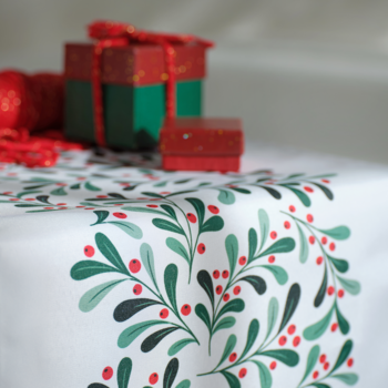 Biały bieżnik świąteczny z zielonym wzorem jemioły i czerwonymi jagodami, z rozmytymi prezentami w tle.