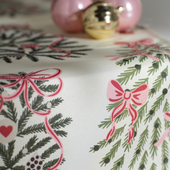 Obrus świąteczny: zielone gałązki, czerwone kokardy i serca na jasnym tle, widok z bliska z bombkami.