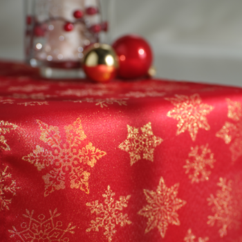 Czerwony satynowy obrus świąteczny ze złotymi śnieżynkami. Widok z bliska, bombki w tle.