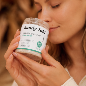 Zbliżenie: kobieta wącha ziołową sól do kąpieli stóp handy lab. Patchouli Mood w słoiku z białą etykietą.