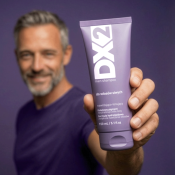 Mężczyzna trzyma fioletowy szampon DX2 Men do włosów siwych, neutralizujący żółte tony. Zbliżenie na produkt.