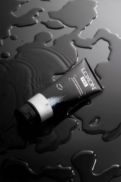 LOXON PRO szampon przeciw wypadaniu włosów w czarnej tubce z srebrną nakrętką, na mokrej, ciemnej powierzchni.