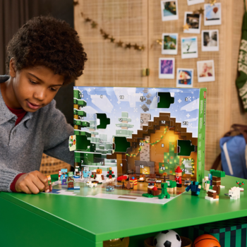 Chłopiec otwiera Kalendarz adwentowy LEGO Minecraft na zielonym stole, ukazujący zimową wioskę i figurki.