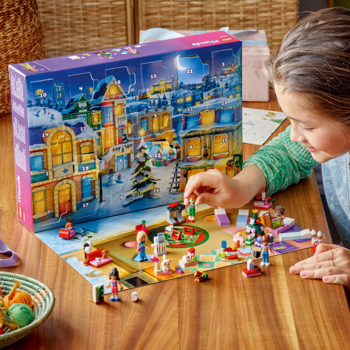 Dziewczynka bawi się elementami LEGO Friends Advent Calendar 2025 na planszy zimowej wioski. W tle pudełko.