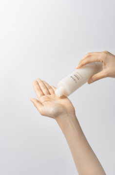 Dłoń wylewa mleczny tonik TIRTIR Milk Skin Toner z białej butelki na otwartą dłoń, zbliżenie.