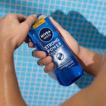 Niebieska butelka szamponu wzmacniającego NIVEA MEN Strong Power w dłoniach, widok z góry, na tle kafelków.