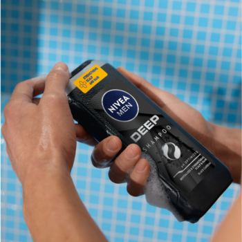 Męski szampon Nivea Men Deep z czarnym węglem w czarnej butelce, spieniony, trzymany w dłoniach pod prysznicem.