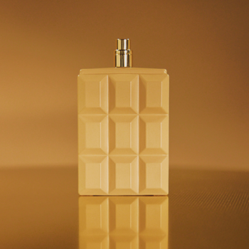 Perfumy Sabrina Carpenter Caramel Dream, beżowa butelka o fakturze czekolady, ze złotym atomizerem, na złotym tle.