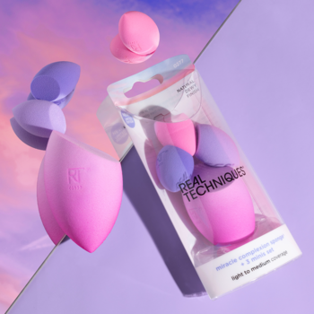 Zestaw gąbek Real Techniques Miracle Complexion: duża różowa, dwie małe fioletowa i różowa, z opakowaniem na fioletowo-różowym tle.