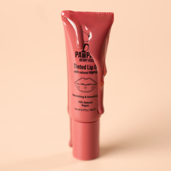 Dr. PawPaw Berry Kiss Tinted Lip Balm w różowej tubce, z błyszczącym olejkiem rozlanym na opakowaniu, pastelowe tło.