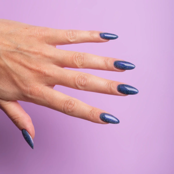 Lewa dłoń z długimi paznokciami Semilac Virtual Blue, holograficzny błękit, migoczące drobinki na tle lila.