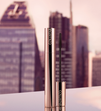 Mini tusz Collistar Mascara Infinito Extra Nero, różowo-złota tuba z otwartą szczoteczką, na tle miasta.
