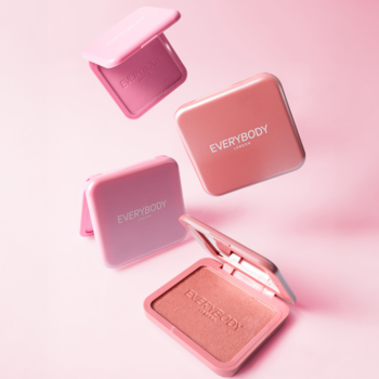 Rozświetlający róż w kamieniu Everybody London Berry Pearl, otwarty, wśród różowych i brzoskwiniowych kompaktów, na różowym tle.