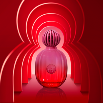 Różowo-czerwona butelka wody perfumowanej Icon Supreme z ryflowanym korkiem, na tle czerwonych, lśniących łuków.