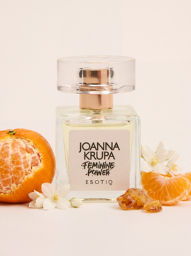 Flakon perfum Esotiq Joanna Krupa Feminine Power z cytrusami i białymi kwiatami na jasnym tle.