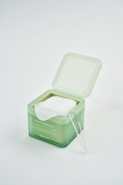 Otwarte, kwadratowe, zielone pudełko płatków z esencją drzewa herbacianego, obok leży przezroczysta pęseta.