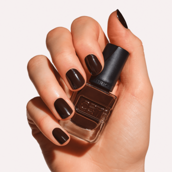 Dłoń z paznokciami w kolorze Double Shot Diva trzyma żelowy lakier Catrice w ciemnobrązowej butelce.