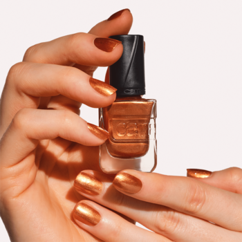 Żelowy lakier Catrice Gel Affair Copper Cabana trzymany dłońmi z miedzianymi paznokciami, butelka, widok z przodu.