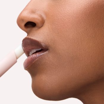 Kobieta aplikuje błyszczyk w sztyfcie Catrice Diamond Glaze Gloss Stick na usta, widok z boku, rozświetlony efekt.