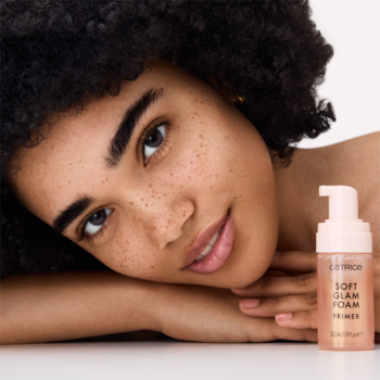 Catrice Soft Glam Foam Primer w różowej butelce z pompką, obok modelki z promienną cerą i piegami.