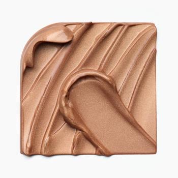 Catrice Bronze Glow Grip Primer Sun Glazed. Kremowy, świetlisty swatch brązowej bazy rozświetlającej na białym tle.