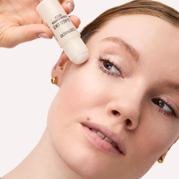 Kobieta aplikuje transparentny rozświetlacz w sztyfcie Catrice Glass Like na policzek, uzyskując efekt tafli szkła.