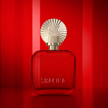 Woda perfumowana Shakira ROJO w rubinowo-czerwonej, kwadratowej butelce ze złotym, plisowanym korkiem SK, na lśniącym czerwonym tle.