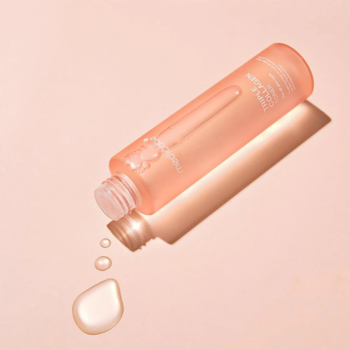 Medicube Triple Collagen Toner w brzoskwiniowej butelce leży pod kątem, z wyciekającym płynem, na różowym tle. Tonik ujędrniający.