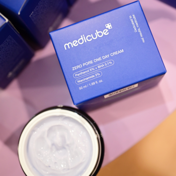 MEDICUBE Zero Pore One Day Cream w niebieskim pudełku obok otwartego słoika z gładkim fioletowym kremem. Z góry.