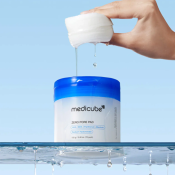 Dłoń podnosi nasączony pad Medicube Zero Pore Pad MILD z białej tubki. Delikatne złuszczanie i zwężanie porów.