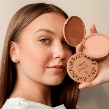 Kobieta prezentuje otwarty i zamknięty bronzer Lumene Natural Glow Arctic Sun, okrągłe opakowania w ciepłym brązie.