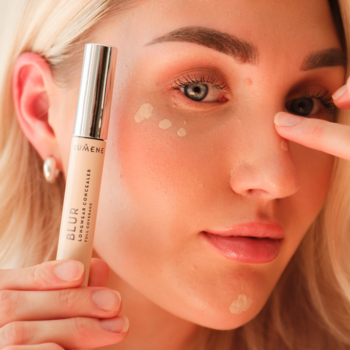 Kobieta nakłada jasny korektor Lumene Blur Light z srebrną zatyczką pod oko i na czoło w kropki.