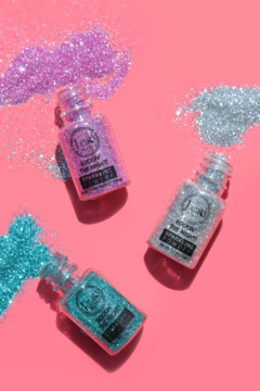 Trzy sypkie brokaty Sparkle Powder: różowy, srebrny i turkusowy, w słoiczkach na różowym tle, widok z góry.