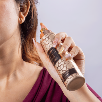 Kobieta spryskująca szyję brązowo-złotym sprayem Oud Elixir z geometrycznym wzorem, zbliżenie dłoni.