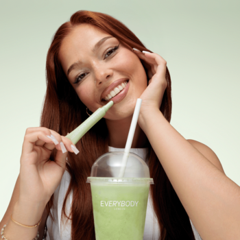 Kobieta z zielonym aplikatorem peptydowego balsamu Matcha Latte; nawilża, odżywia usta, na tle zieleni.