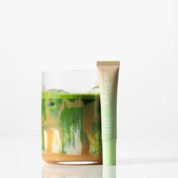 Balsam do ust Peptide Lip Balm Caramel Matcha w beżowo-zielonej tubce stojącej obok szklanki z matcha latte.