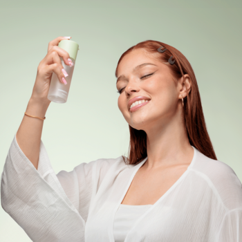 Młoda kobieta z uśmiechem aplikuje odświeżającą mgiełkę Everybody London Energizing Spray z matchy na twarz.