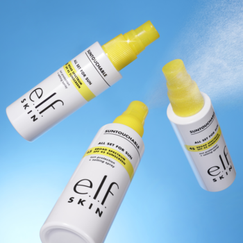 Trzy białe butelki e.l.f. SKIN Suntouchable Whoa Glow SPF 30 unoszą się na niebieskim tle, z widoczną mgiełką sprayu.
