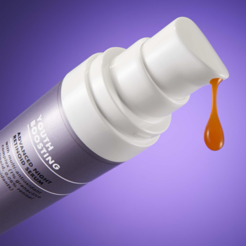 Youth Boosting Advanced Night Serum z retinoidami, biała butelka z fioletową etykietą, kropla pomarańczowego serum. Widok pod kątem, na fioletowym tle. Redukuje zmarszczki.