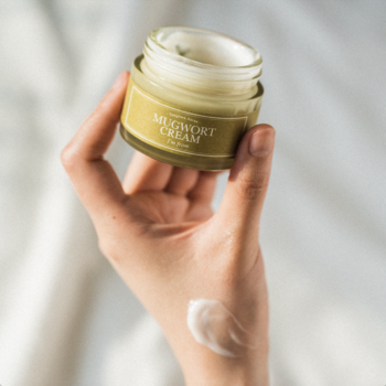 I'm From Mugwort Cream, kojący krem do twarzy z bylicą, w zielonkawym słoiczku, z próbką produktu na dłoni.