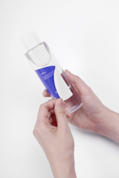 Dłonie trzymają butelkę toniku nawilżającego Isntree Hyaluronic Acid z niebieską etykietą na białym tle.