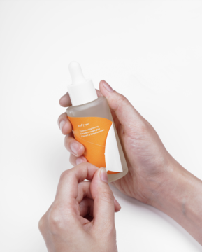 Ręce odklejają etykietę z butelki Isntree C-Niacin Toning Ampoule, rozświetlającej ampułki z witaminą C.