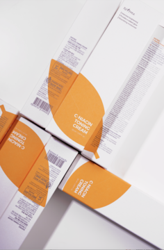 Rozświetlający krem Isntree C-Niacin Toning Cream. Kilka białych opakowań z pomarańczowym wzorem, widok z góry.