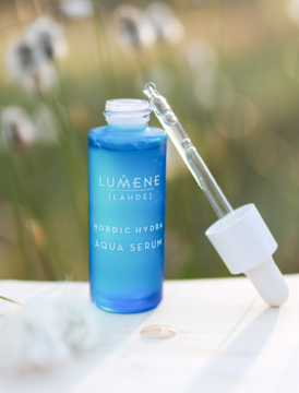 Nawilżające serum Lumene Nordic Hydra w niebieskiej butelce z aplikatorem, pod kątem, na jasnym, rozmytym tle.